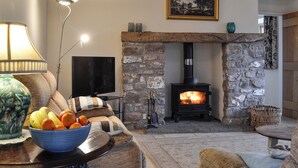 A cozy living room with a stone fireplace, a television, and a bowl of fruit on a table. - 3 bedroom accommodation in Middleton, near Swansea (Middleton, near Swansea)
