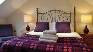 A bedroom with a sloped ceiling, a bed with a metal headboard, two bedside lamps, and a purple patterned bedspread. - 3 bedroom accommodation in Middleton, near Swansea (Middleton, near Swansea)