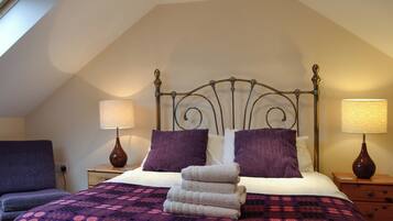 A bedroom with a sloped ceiling, a bed with a metal headboard, two bedside lamps, and a purple patterned bedspread.