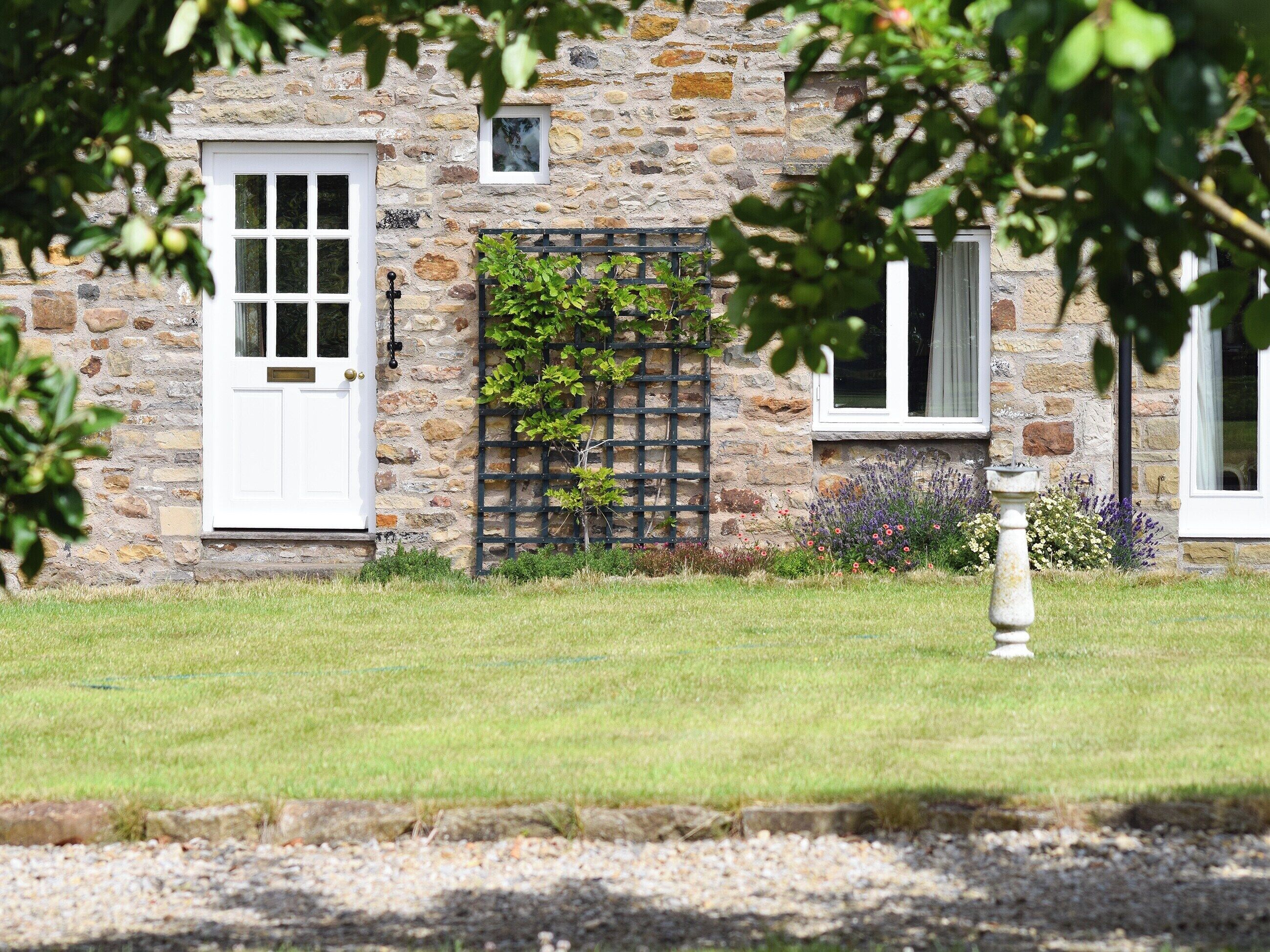 A stone building with a white door and windows, surrounded by a well-maintained lawn and a small garden with flowers.
