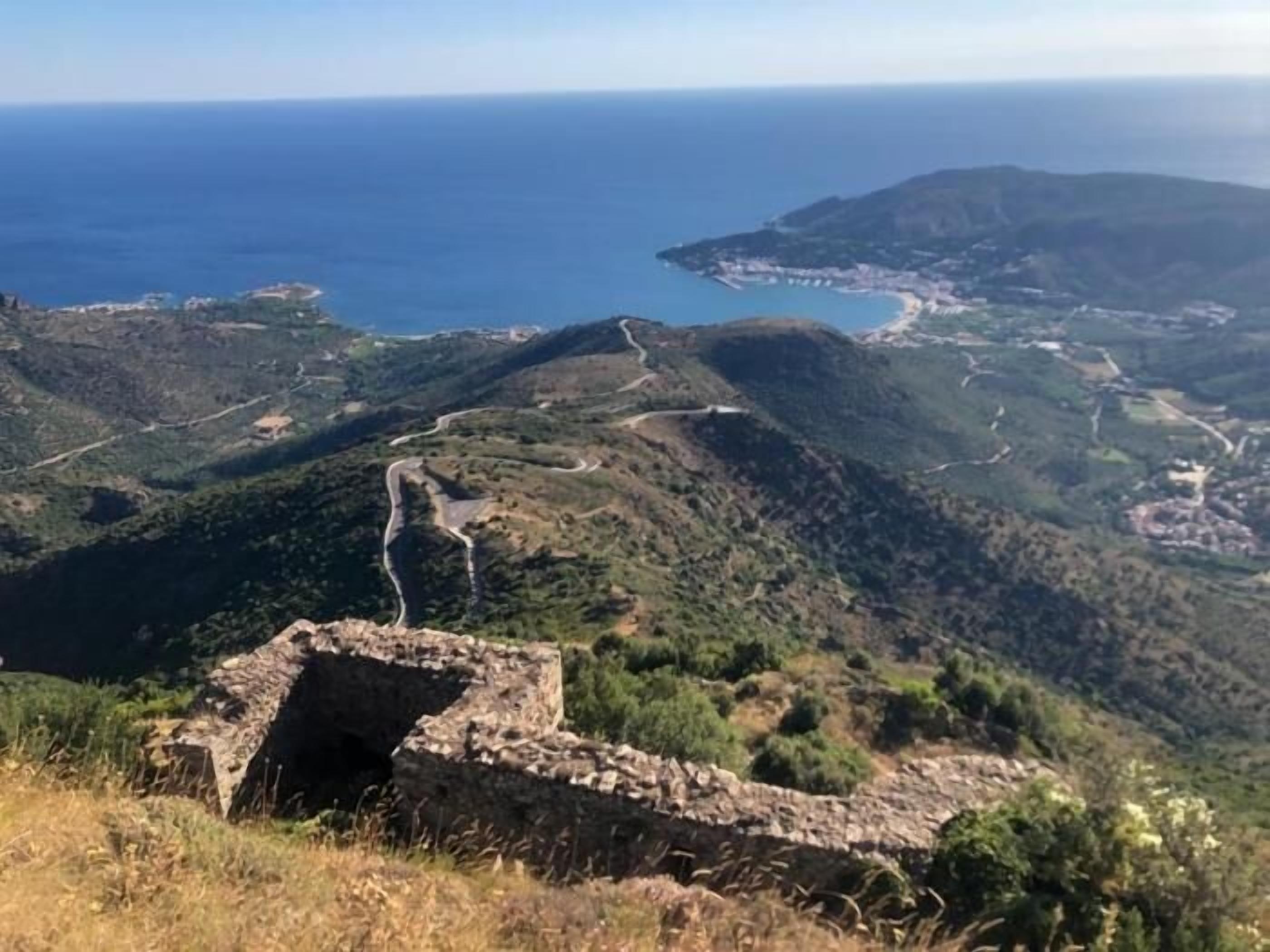 A mountainous landscape with a winding road, a stone structure, and a coastal view.