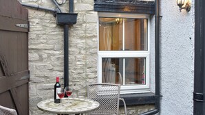Un edificio de piedra con una ventana, una mesa con sillas y una botella de vino.