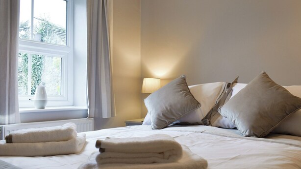 Una habitación de hotel con una cama bien hecha, dos almohadas, una lámpara de noche y una ventana con cortinas.