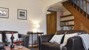 Una sala de estar con sofás de cuero, una mesa de centro de madera con copas de vino y una botella, cuadros en la pared, una lámpara y una estantería.