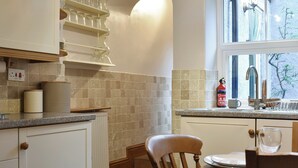 Una cocina con armarios blancos, una silla de madera, una mesa de comedor y una ventana con vistas a árboles.