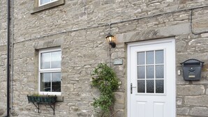 Un edificio de piedra con una puerta blanca, una ventana con marco blanco y una pequeña señal sobre la puerta que dice 