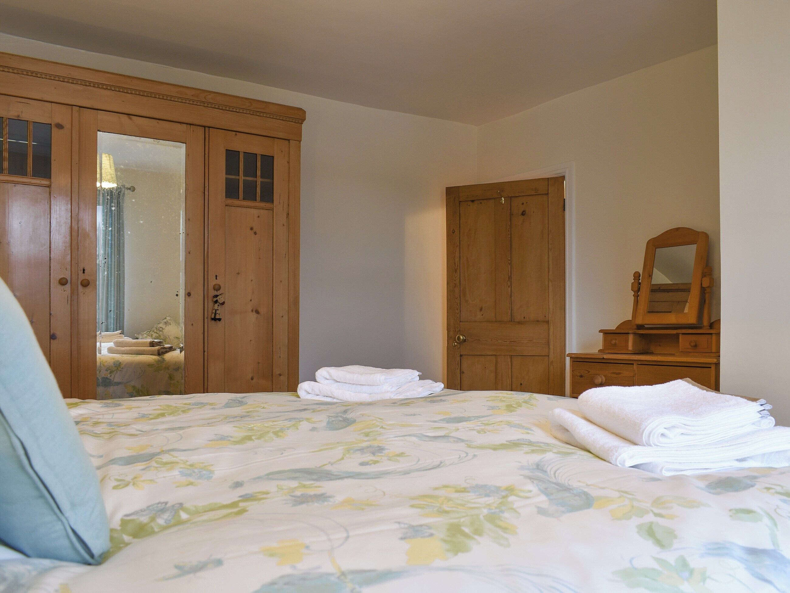 A bedroom with a bed, a wooden wardrobe, a mirror, and a dresser.