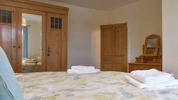 A bedroom with a bed, a wooden wardrobe, a mirror, and a dresser.