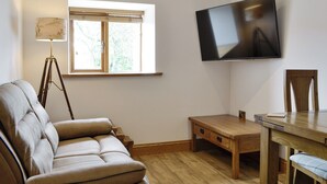 Een woonkamer met een bank, een houten tafel, een aan de muur bevestigde televisie en een raam met jaloezieën.