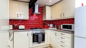 Una cocina con armarios blancos, salpicadero de baldosas rojas, estufa a gas, microondas y campana extractora de acero inoxidable.