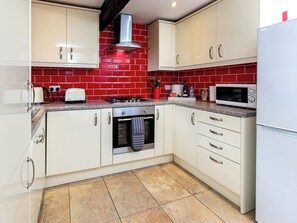 A kitchen with white cabinets, a red tiled backsplash, a gas stove, a microwave, and a stainless steel range hood.