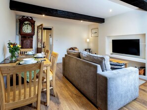 A modern living room with a wooden dining table, a sofa, a flat-screen TV, and a wall-mounted clock.