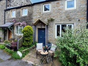 A stone house with a blue door, a small garden, and outdoor seating.