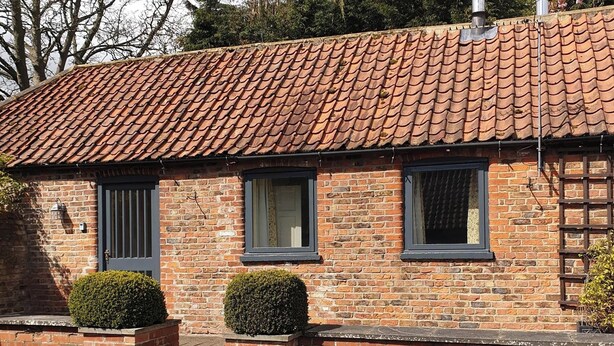 A brick house with a tiled roof, two windows, and two small bushes in front. - 1 bedroom accommodation in Fitling, near Hull (Fitling, near Hull)