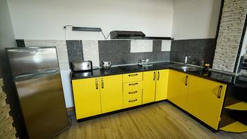Una cocina con armarios amarillos, un refrigerador de acero inoxidable y una encimera negra.