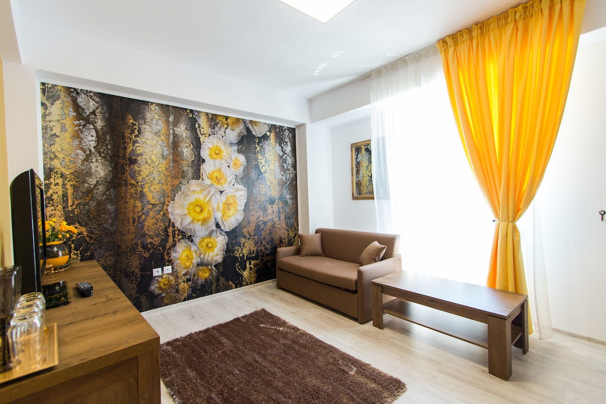 Een moderne woonkamer met een bruine bank, een houten salontafel en een groot abstract schilderij aan de muur.