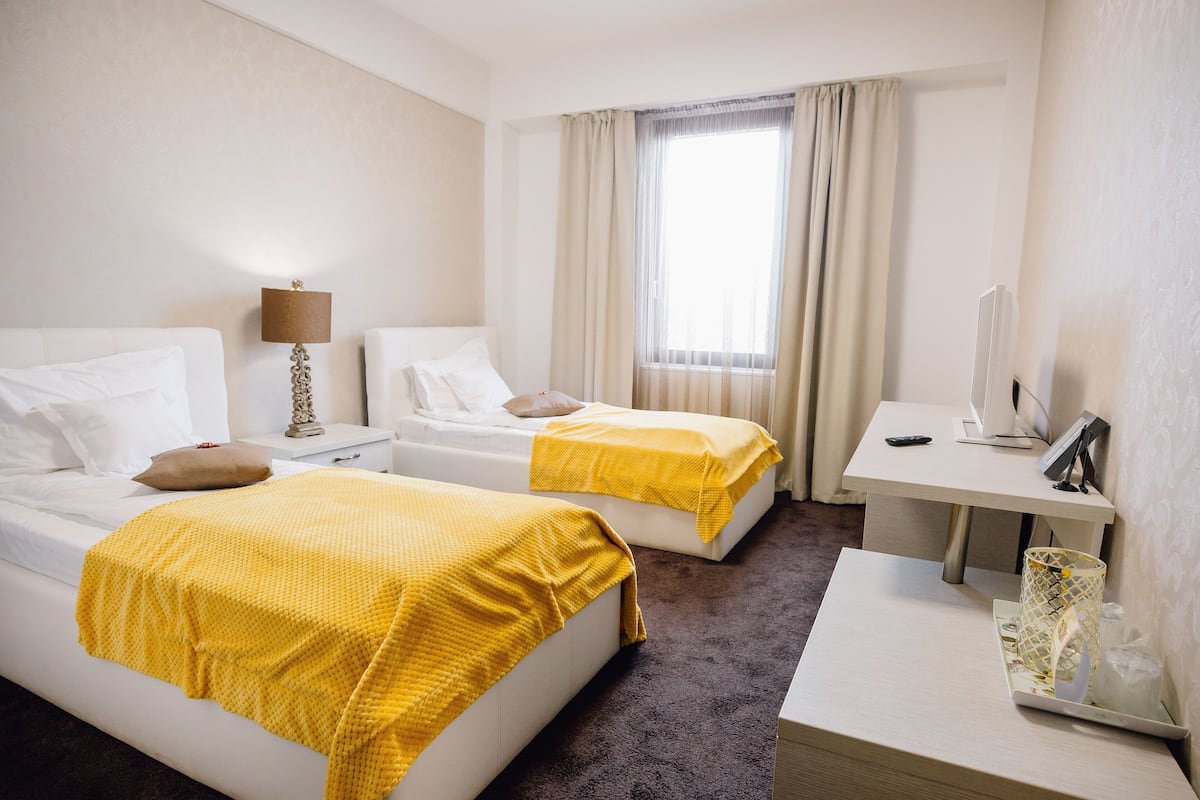 Een hotelkamer met twee bedden, een bureau, een lamp en een raam met gordijnen.