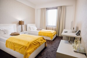 Ein Hotelzimmer mit zwei Betten, einem Schreibtisch, einer Lampe und einem Fenster mit Vorhängen.