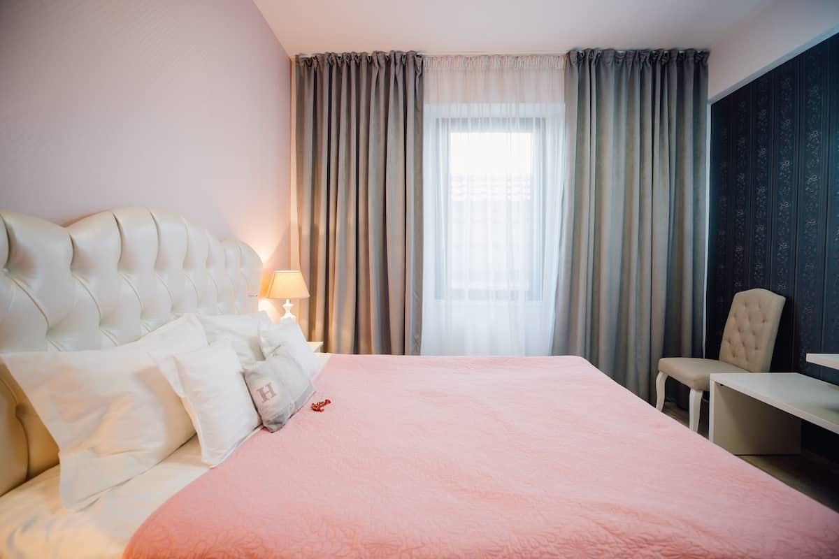 Een hotelkamer met een groot bed, nachtkastje, stoel en raam met gordijnen.