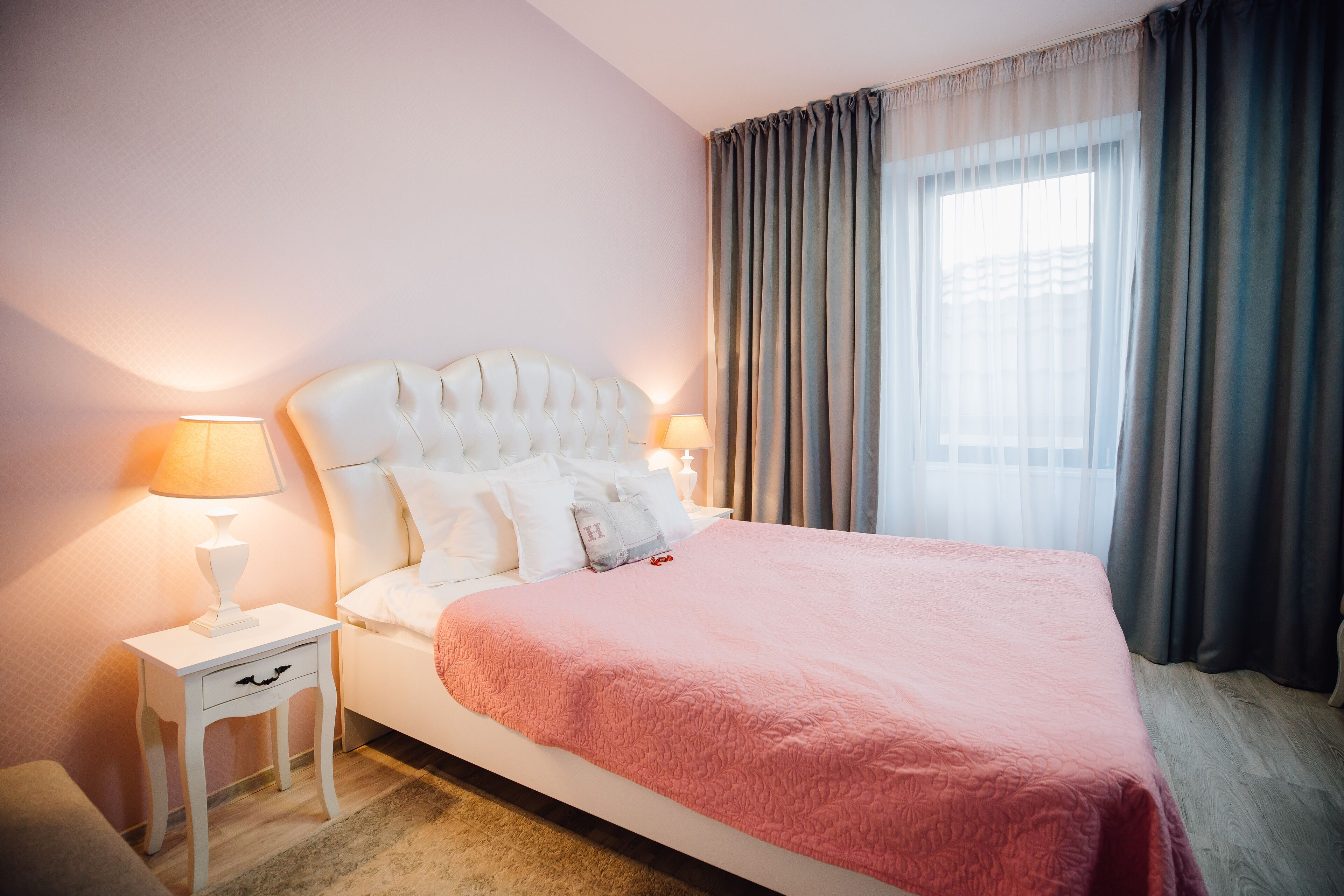 Una cama bien hecha con una manta rosa, dos lámparas de noche y una mesita de noche con una lámpara.
