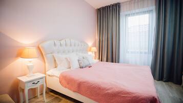 Una cama bien hecha con una manta rosa, dos lámparas de noche y una mesita de noche con una lámpara.