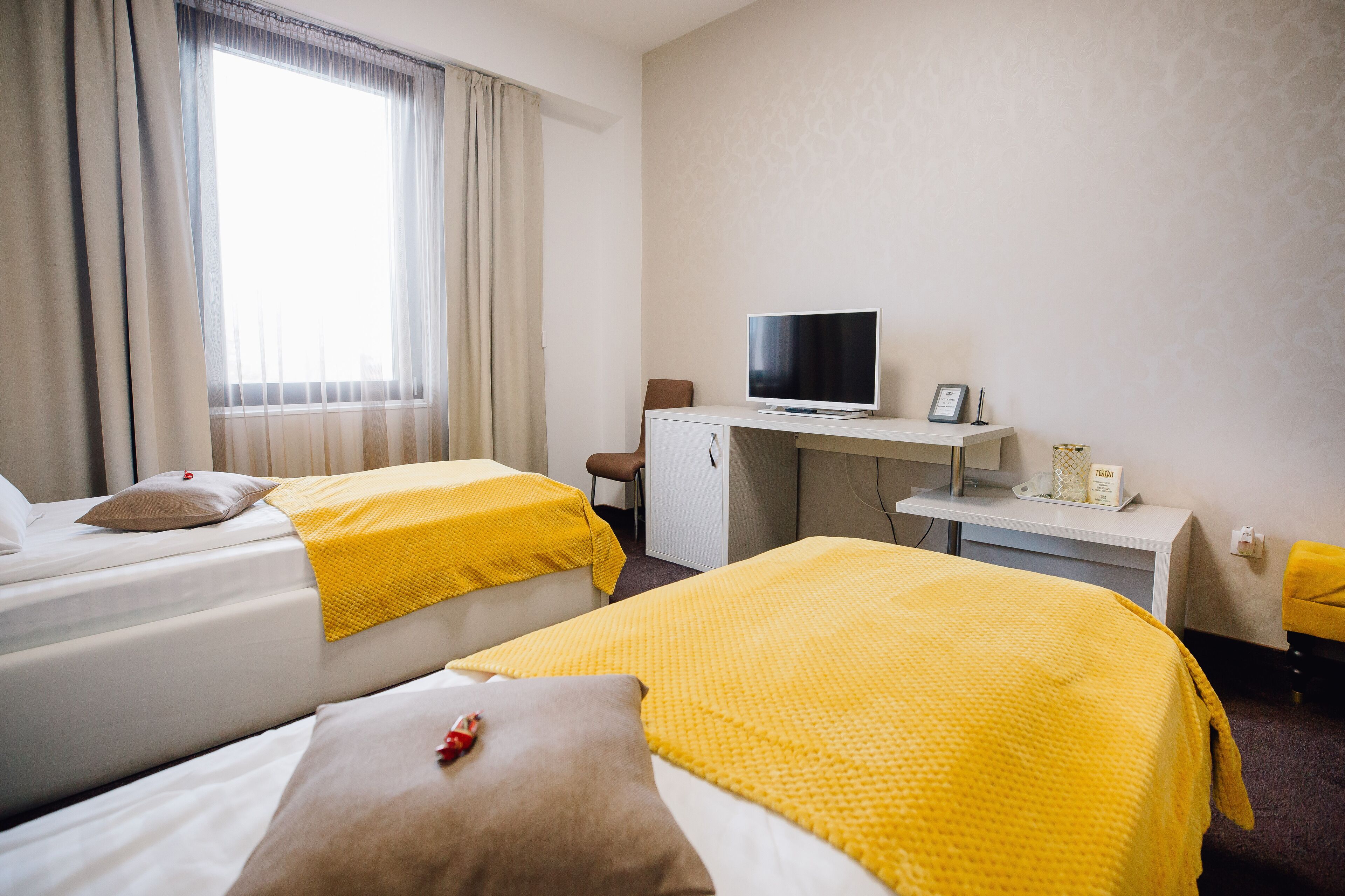 Hotellihuone, jossa on kaksi sänkyä, työpöytä, jossa on televisio, ja ikkuna, jossa on verhot.