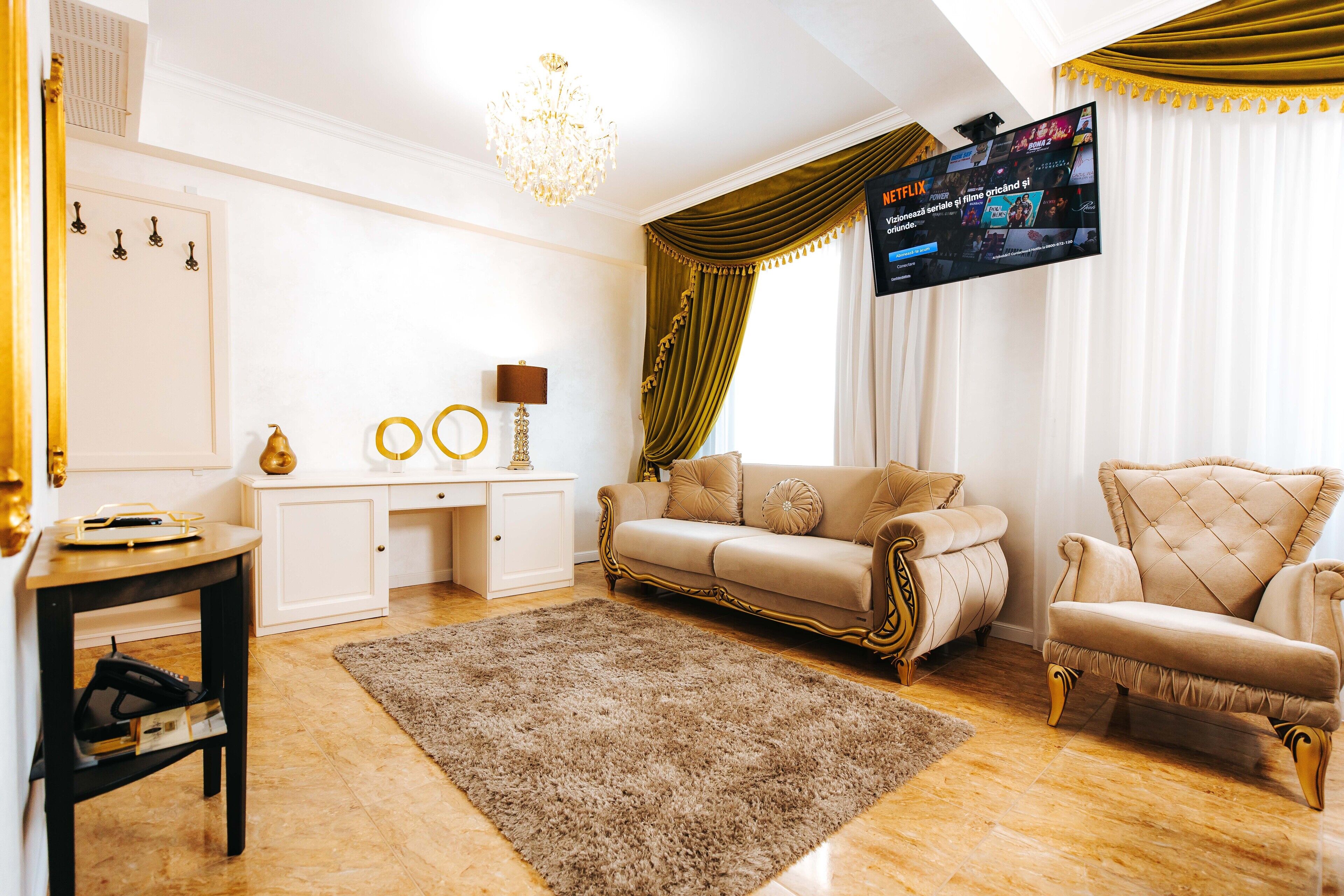 Una sala de estar con un sofá color beige, un sillón a juego, un televisor de pantalla plana montado en la pared y una araña.