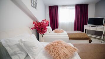 A hotel room with two beds, a TV, a desk, and a window with curtains.