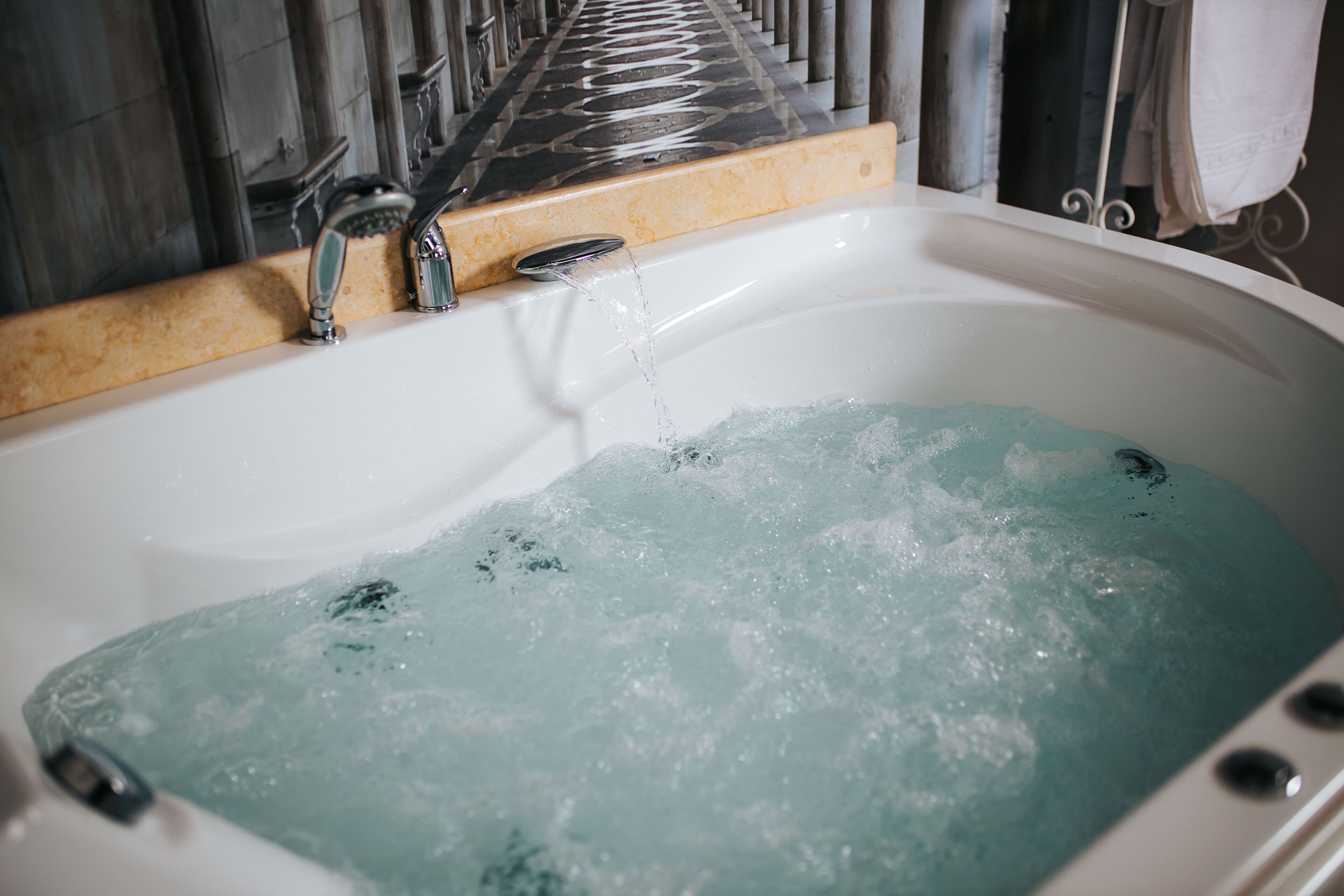 A bathtub with running water, a showerhead, and a tiled wall.