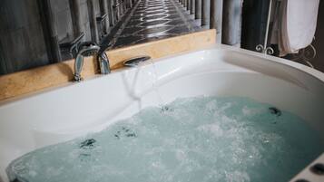 A bathtub with running water, a showerhead, and a tiled wall.