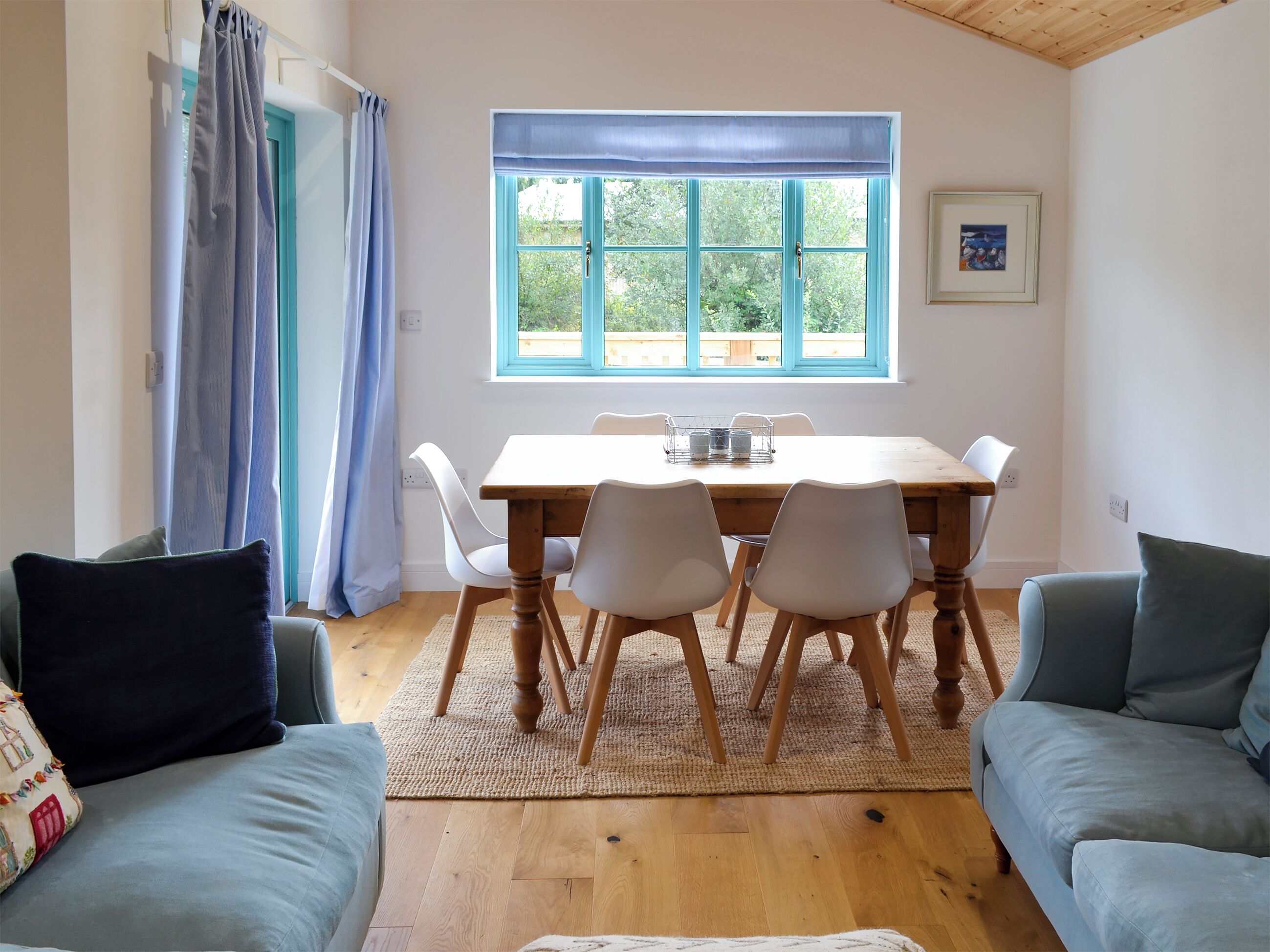 A dining area with a wooden table and chairs, a window with blue shutters, and a view of greenery outside.
