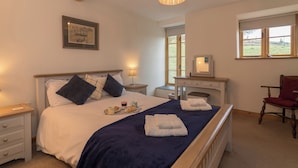 Een slaapkamer met een bed, nachtkastje, lamp, dressoir, stoel en een raam met uitzicht.