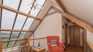 Een loft-achtige kamer met een houten vloer, een rode fauteuil, een klein houten tafeltje met een fles en glas, en uitzicht door grote ramen.
