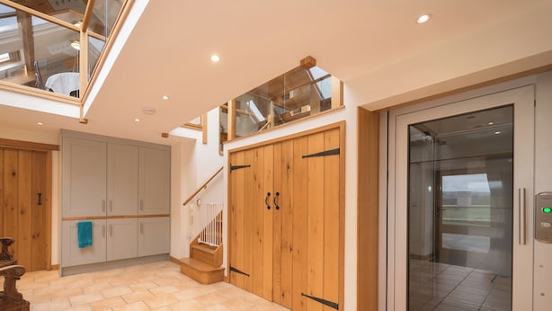 Een ruim interieur met een trap, een houten garderobe en een glazen lift.