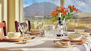 A dining table set for a meal with a scenic mountain view through the window. - 2 bedroom accommodation in Howbeg (Tobha Beag), Isle of South Uist (Howbeg (Tobha Beag), Isle of South Uist)