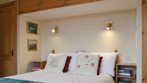 A bedroom with a bed, wooden headboard, bedside tables, wall-mounted lights, and a bookshelf. - 2 bedroom accommodation in Howbeg (Tobha Beag), Isle of South Uist (Howbeg (Tobha Beag), Isle of South Uist)