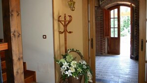 A hallway with a wooden coat rack, a wall-mounted light fixture, and a floral arrangement. - Posada el Hidalgo Mingucho (Medio Cudeyo)
