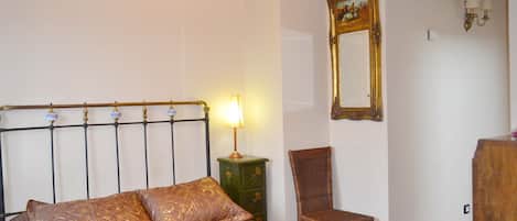A bedroom with a bed, a nightstand, a chair, a mirror, and a lamp.