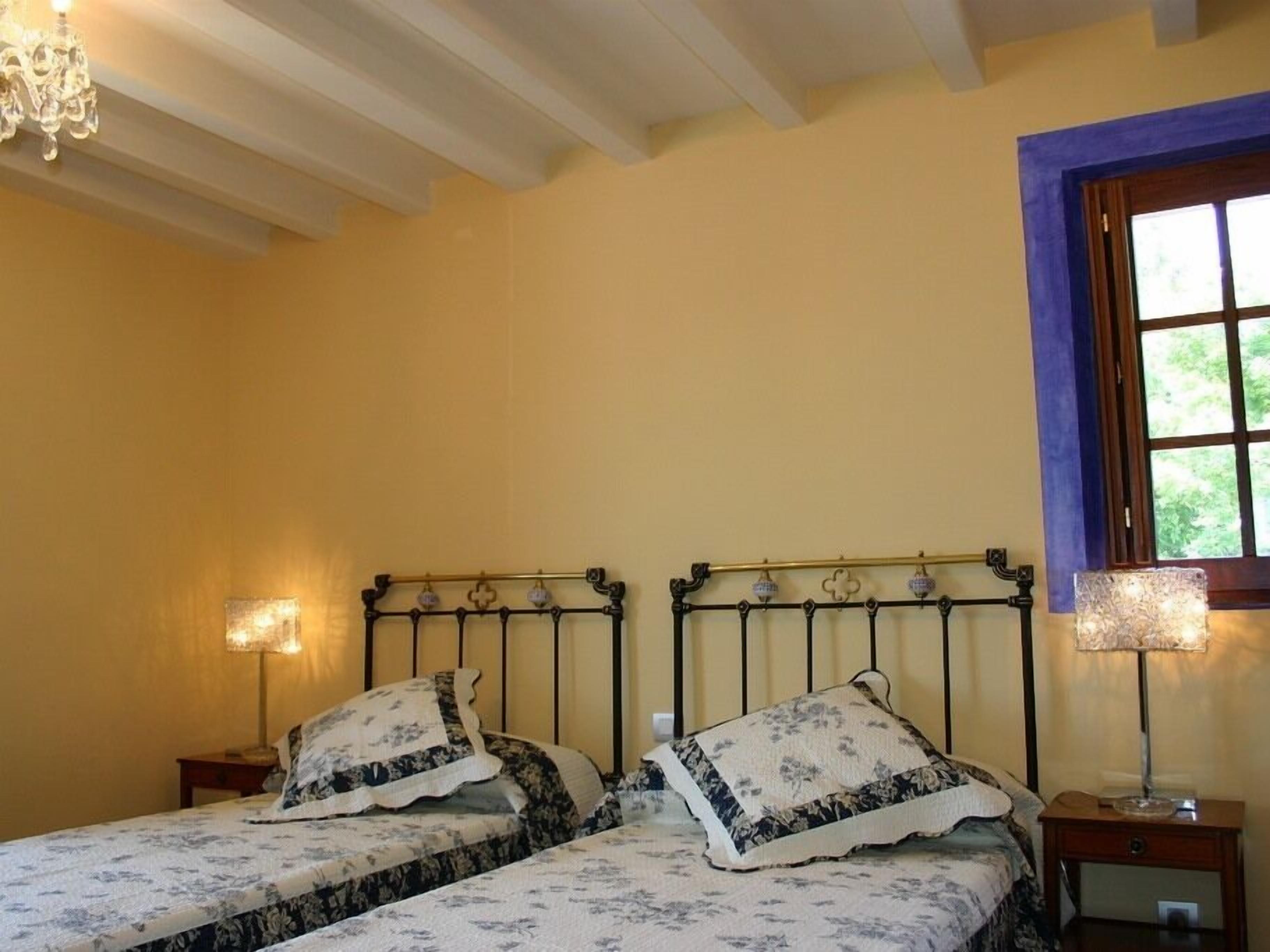 A bedroom with two beds, each with floral-patterned bedding and matching pillows. There are bedside lamps and a chandelier.