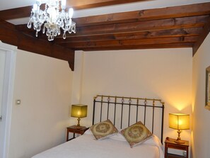 A bedroom with a wooden ceiling, a chandelier, two bedside lamps, a bed with floral pillows, and a small nightstand with a lamp. - Posada el Hidalgo Mingucho (Medio Cudeyo)
