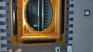 Un baño con espejo en marco dorado, pared con azulejos y zona de lavamanos con artículos de tocador.