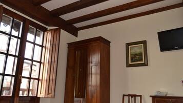 Una stanza con travi in legno al soffitto, un grande armadio in legno, un quadro incorniciato al muro e un televisore sopra un comò.