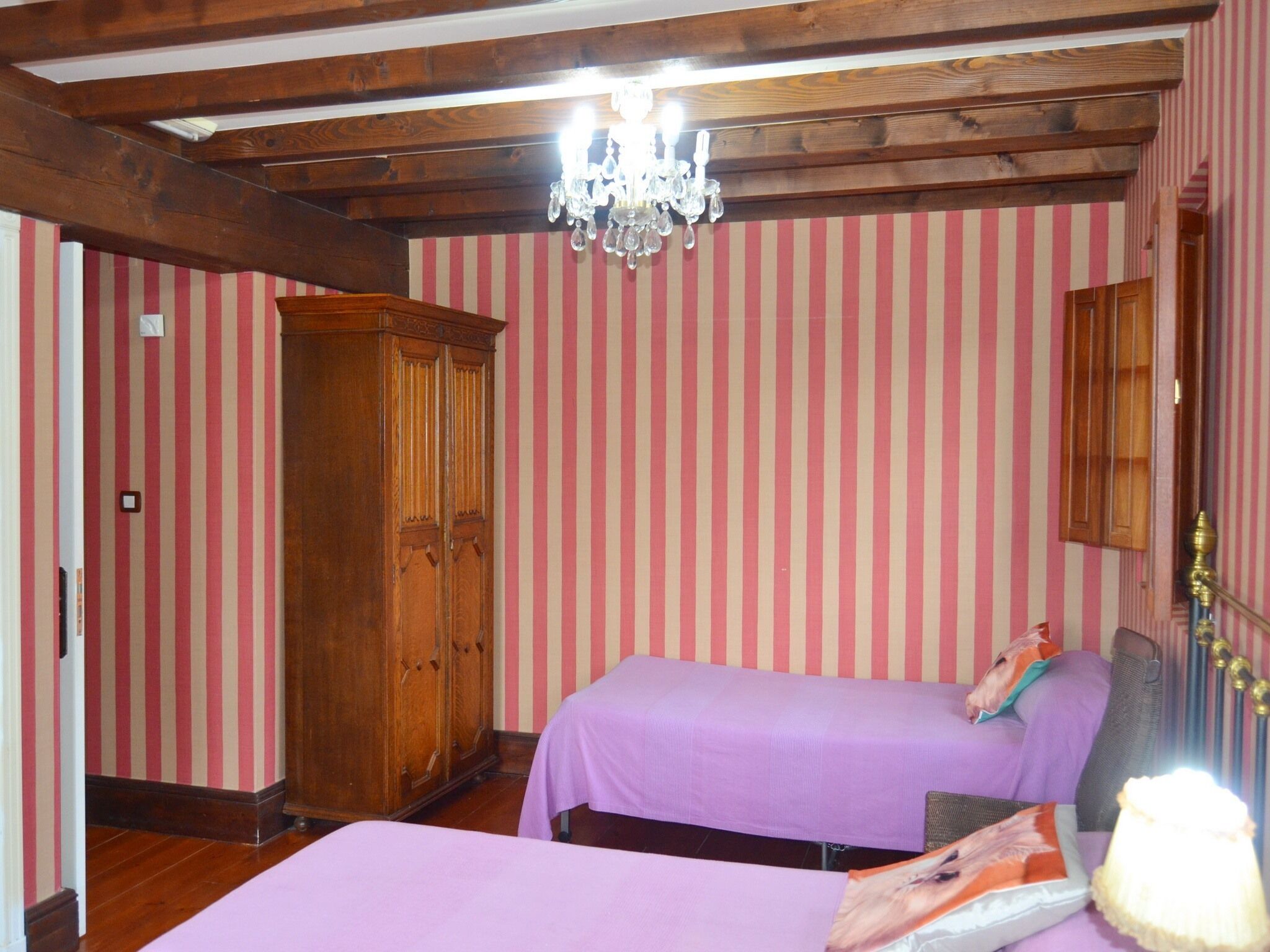 Een kamer met twee bedden, een houten garderobe en een kroonluchter.