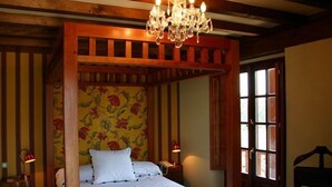 A four-poster bed with a floral wallpaper headboard, a chandelier, and two bedside lamps. - Posada el Hidalgo Mingucho (Medio Cudeyo)