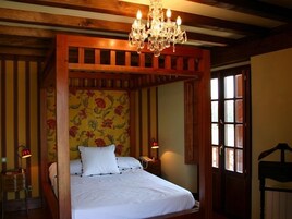 Uma cama de dossel com cabeceira revestida de papel de parede floral, um candelabro e duas luminárias de apoio.