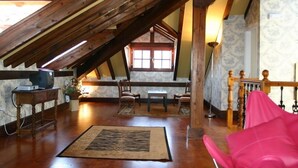 A cozy attic room with wooden beams, a sloped ceiling, a wooden table, chairs, a pink chair, and a television. - Posada el Hidalgo Mingucho (Medio Cudeyo)