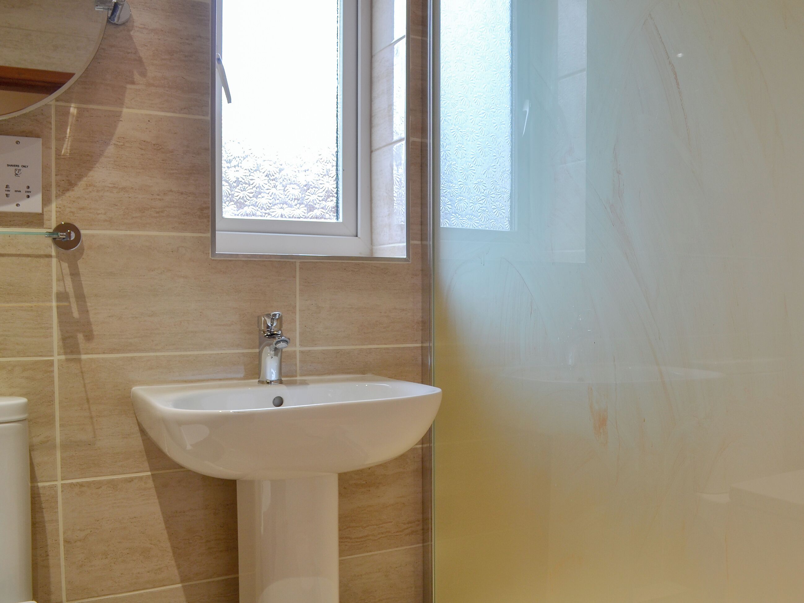 Un baño con un lavamanos blanco, una ventana y zona de ducha.