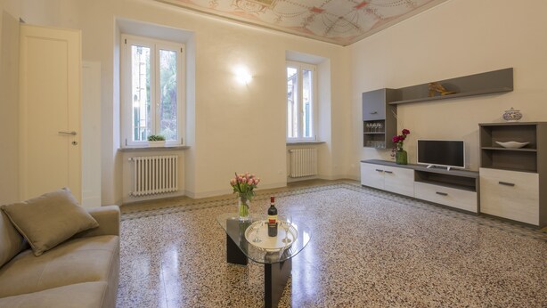 A spacious living room with a glass coffee table, a sofa, a TV, and a decorative shelf. - Few Steps from the Duomo - Luxury Penthouse (Siena)