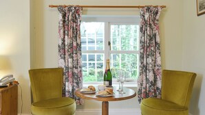 Ein Zimmer mit zwei grünen Sesseln, einem Holztisch mit Champagner, einem Glas und Gebäck.