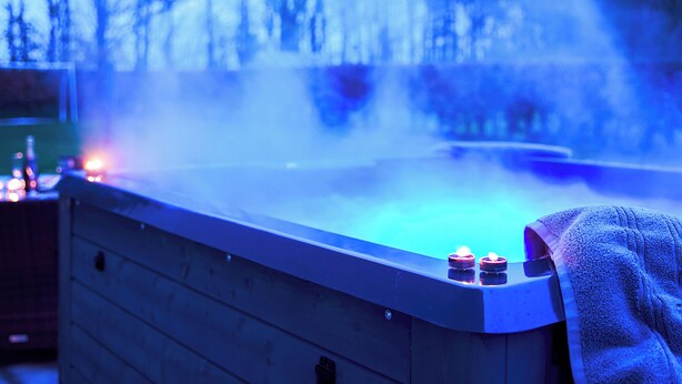 A hot tub with a wooden edge and two lit candles on it.